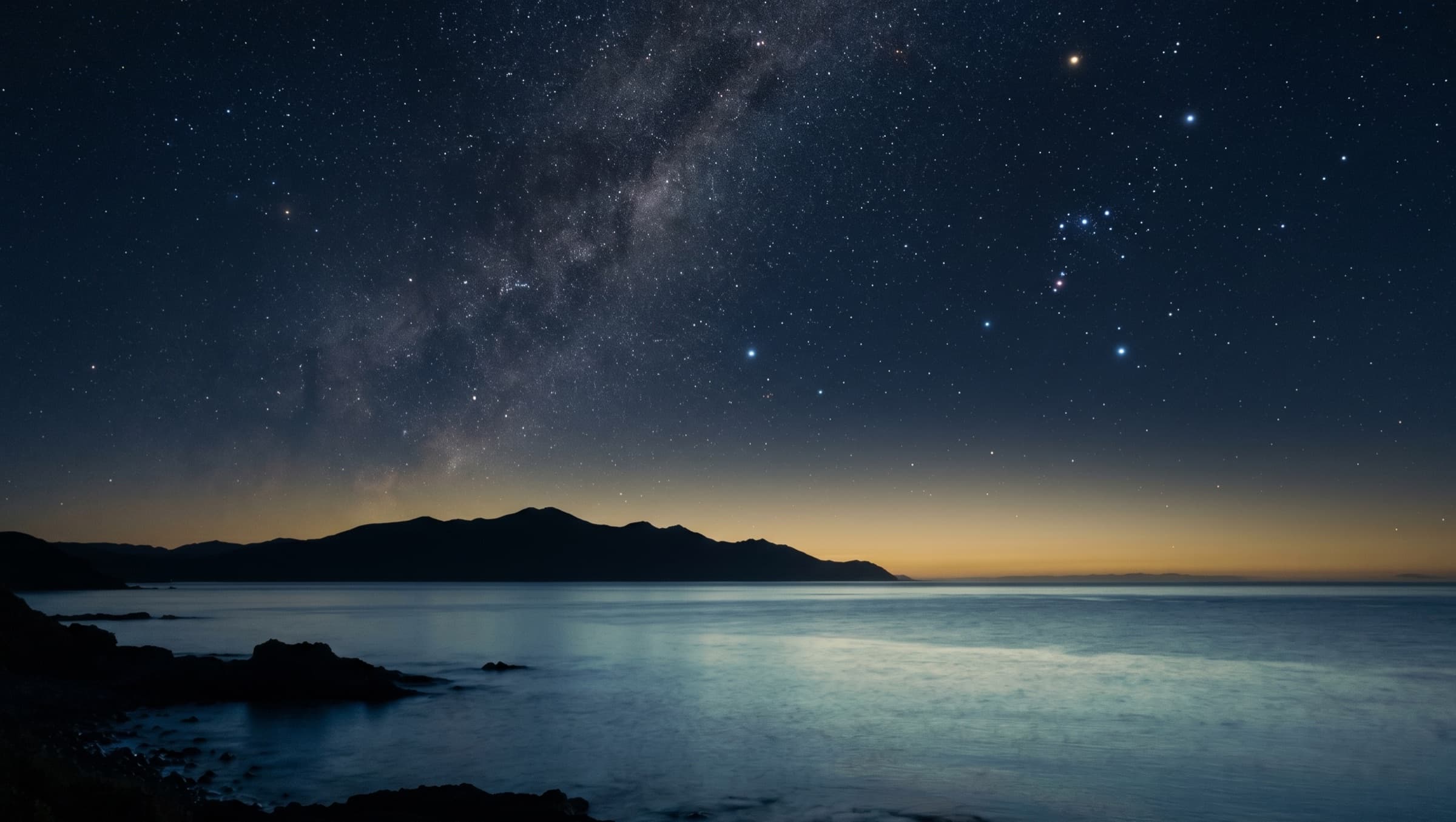 The three stars of Orion's Belt over a calm ocean and a low mountain horizon at night